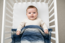 Load image into Gallery viewer, Baby with sleeves lying in crib with Rowan Jeans blanket